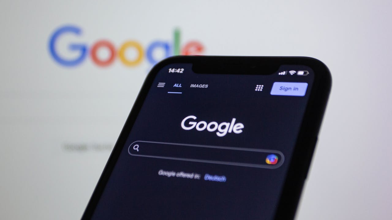 hero-img-02 Smartphone screen showing Google search in dark mode with the Google logo in the background.